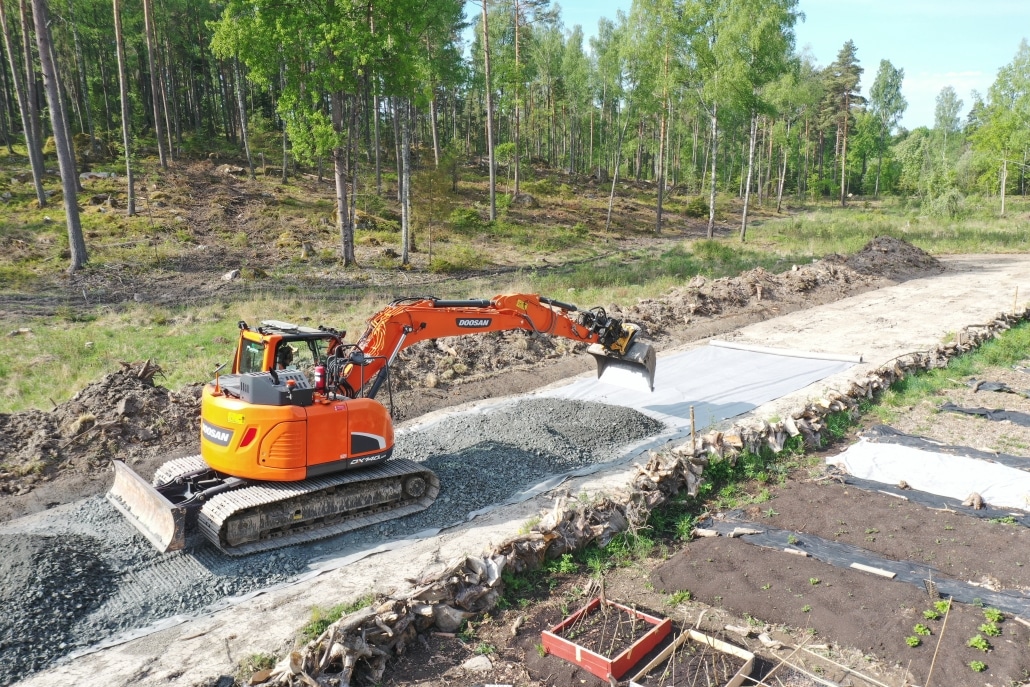 Röd grävmaskin anlägger grusväg i skogsområde