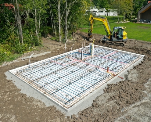 Anläggning av husgrund, betongplatta, med grävmaskin i bakgrund