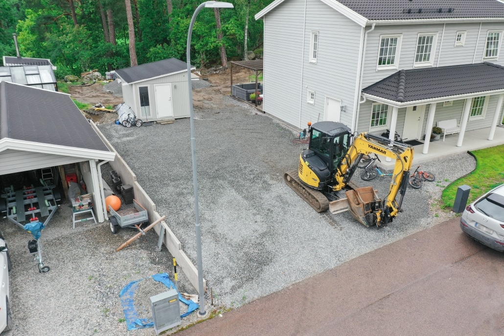 Gul minigrävare står parkerad vid arbetsplats för uppfart bredvid ett bostadshus