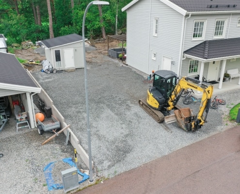 Gul minigrävare står parkerad vid arbetsplats för uppfart bredvid ett bostadshus