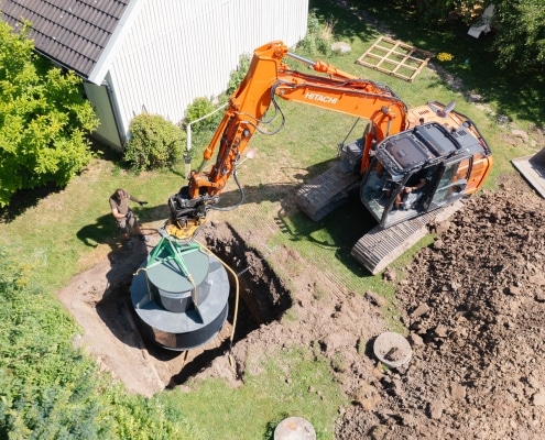 Grävmaskin släpper ner ett minireningsverk i marken.